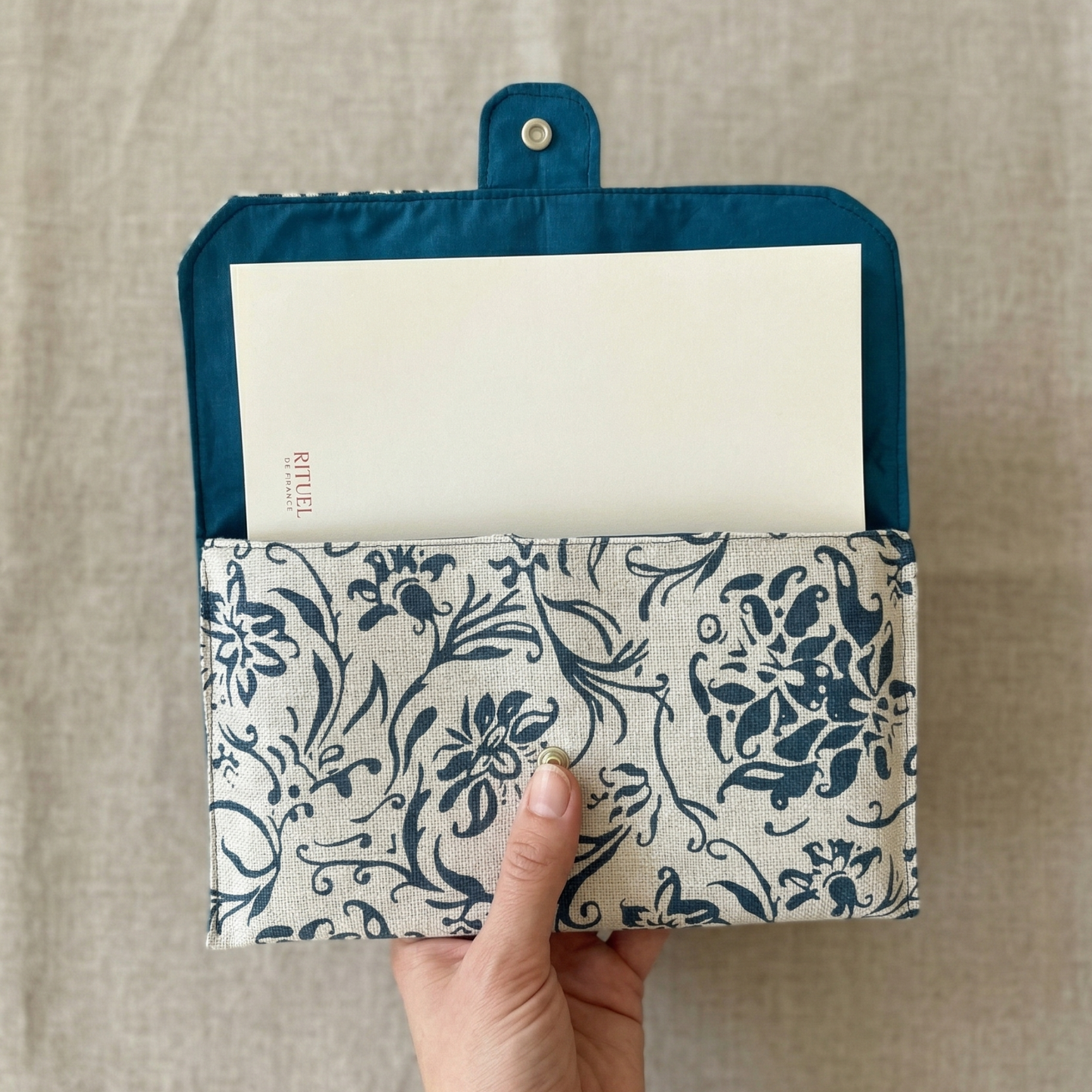 Main tenant la pochette artisanale Marine avec carnet MAMAN personnalisé glissé à l'intérieur — cadeau fête des mères